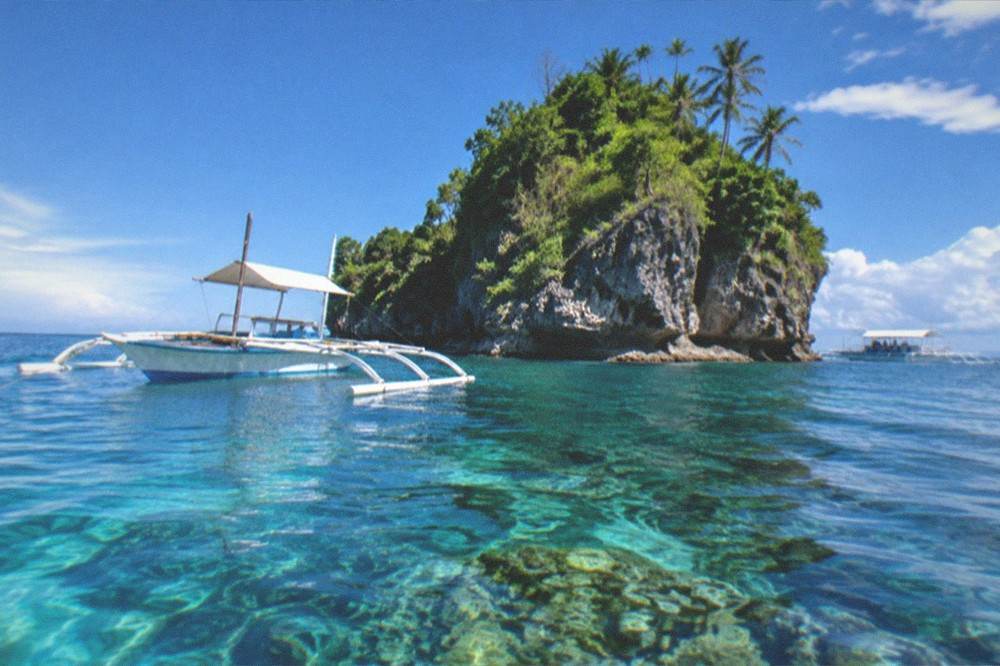 A small outrigger boat anchored over clear water beside a reef drop-off