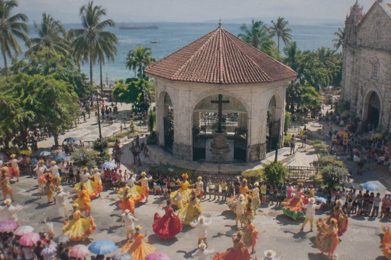 Crowds in colorful festival costumes dancing through a city street under a bright tropical sky
