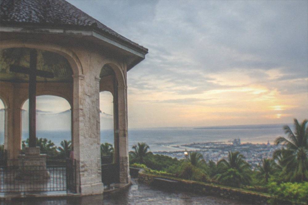 A hilltop lookout at dusk with city lights spreading along a coastal plain below