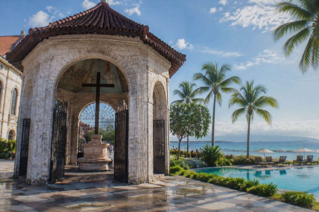 A resort swimming pool beside a calm tropical beach with palm trees and loungers
