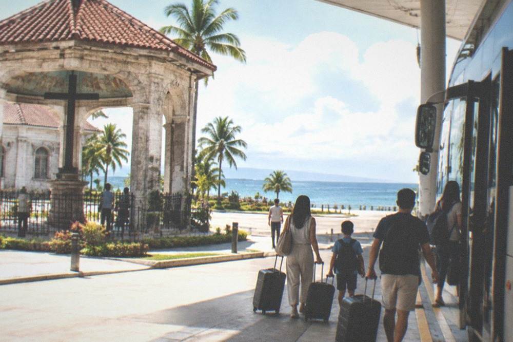 A family with luggage boarding an air-conditioned bus at a tropical airport curb