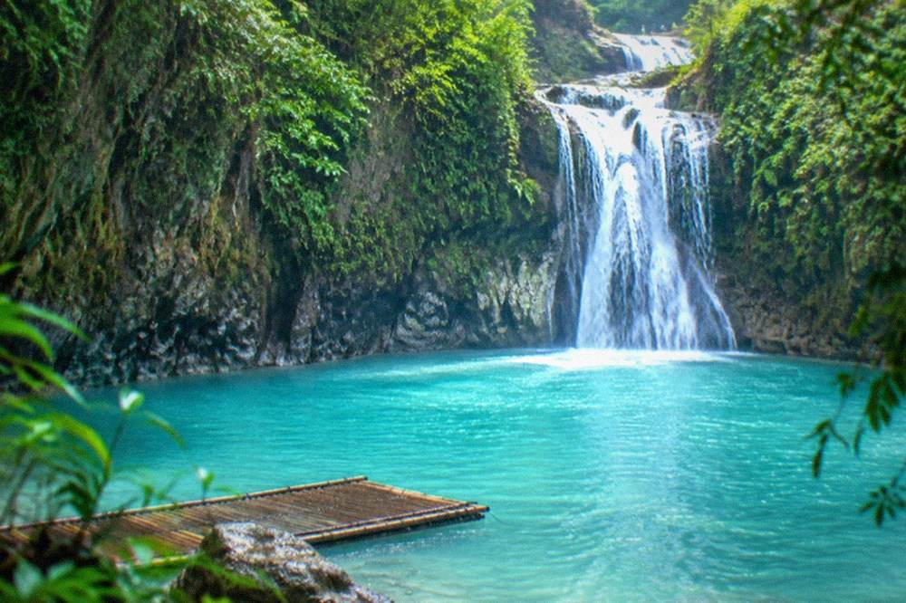 Turquoise pool at the base of Kawasan Falls surrounded by jungle and a bamboo raft