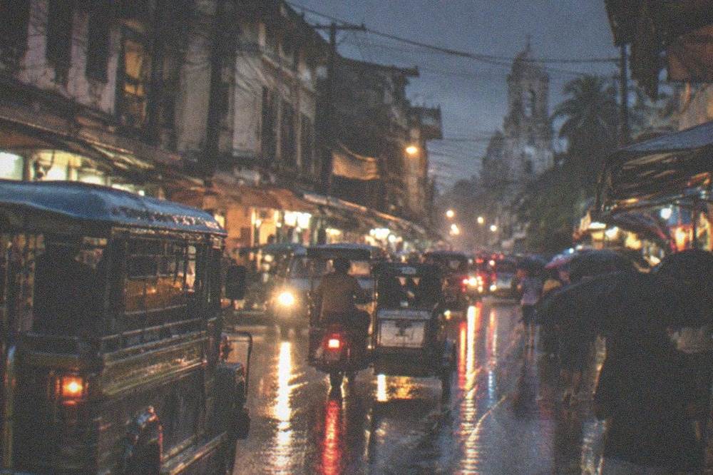 A rainy city street at night with reflections of neon signs on wet pavement