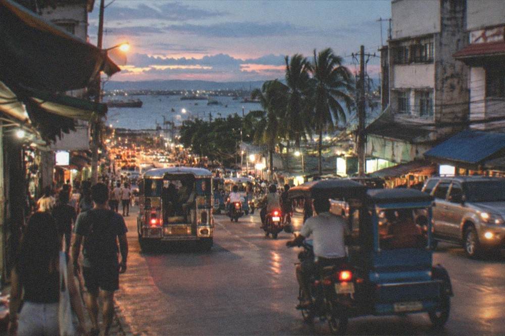 A wide view of a tropical city at night with scattered lights along a dark coastline