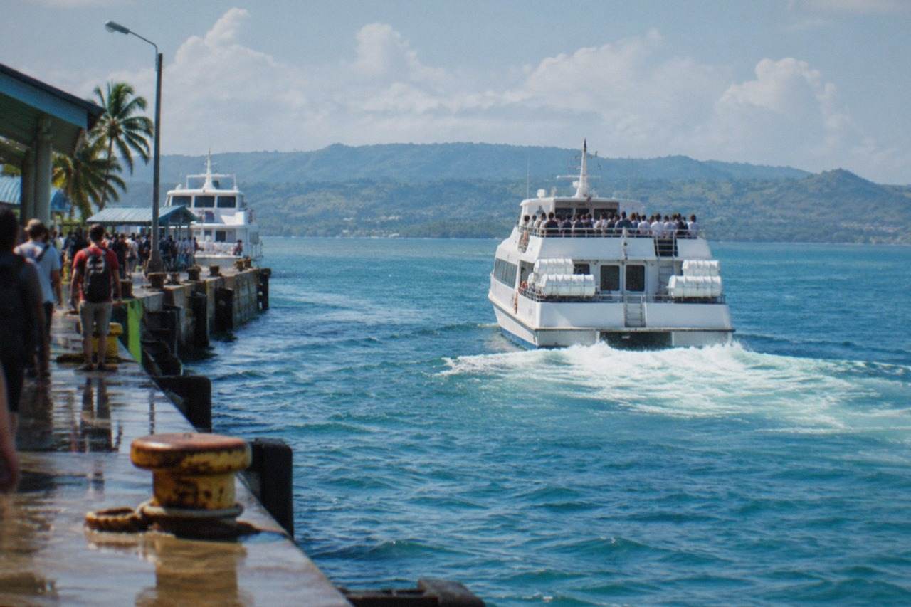 A white fastcraft ferry loaded with passengers pulling away from a busy city pier in the Philippines