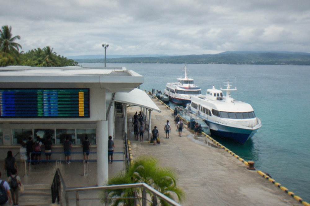 A departures board listing ferry times above a ticket window at a Philippine port terminal