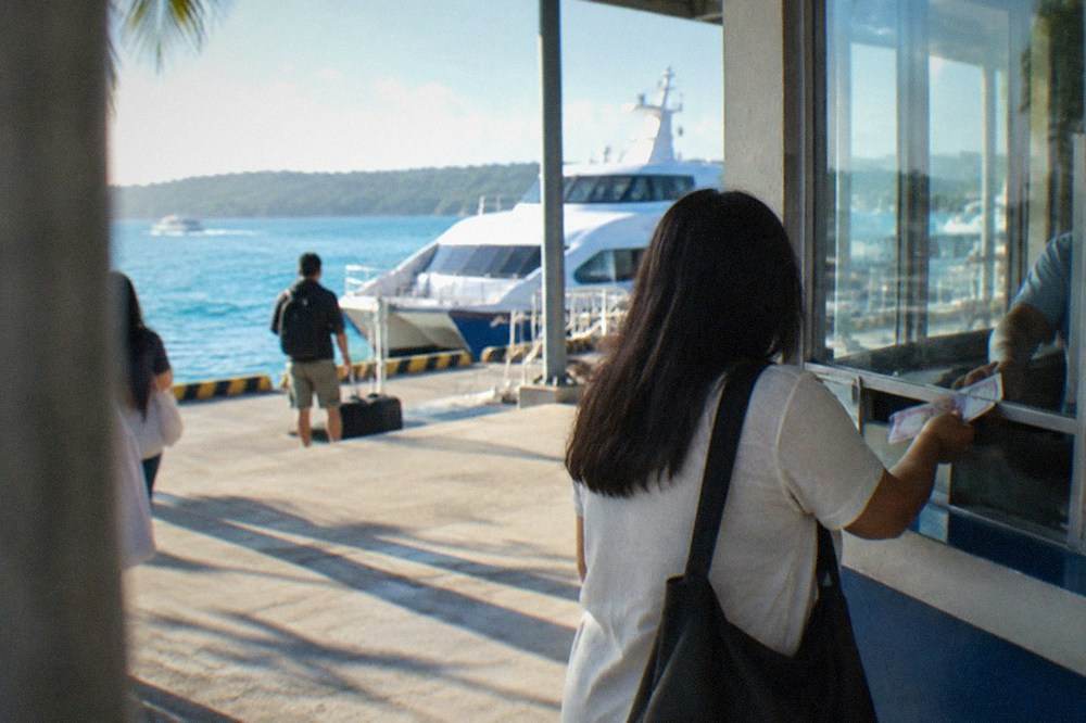 A passenger handing peso banknotes to a clerk at a ferry ticket counter window