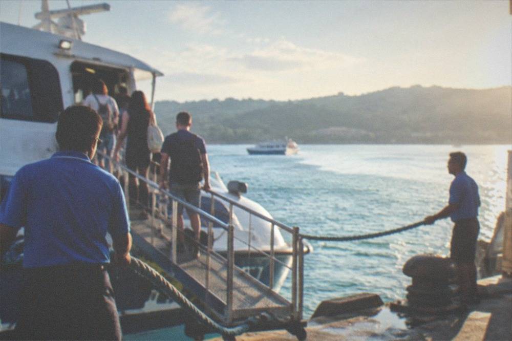 Tourists boarding a fast ferry via a gangway at a Philippine port while crew members hold the ropes
