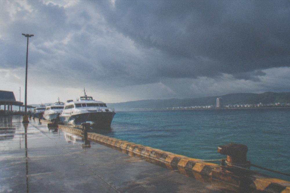 Dark storm clouds gathering over a coastal city skyline and an empty ferry terminal