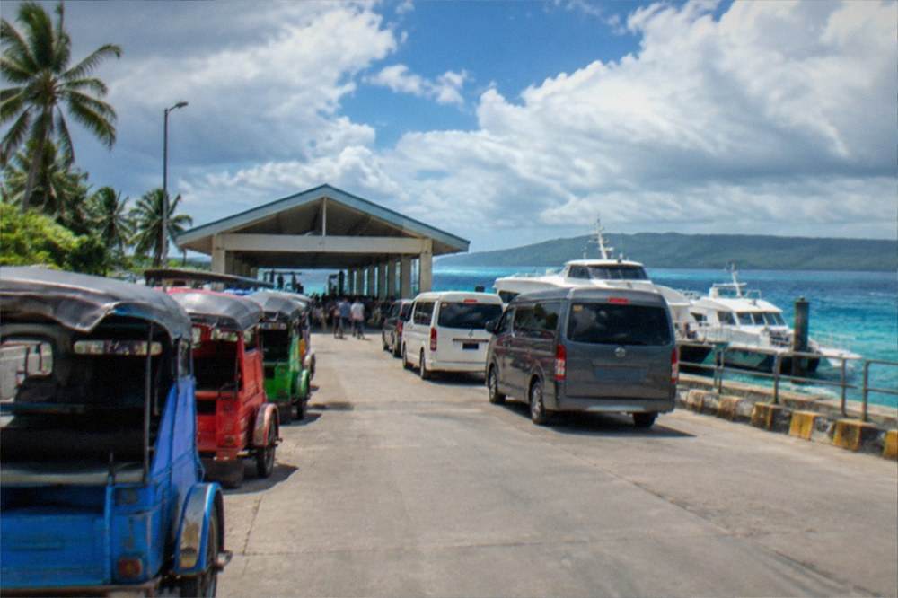 A line of colorful tricycles and vans waiting outside a small island port terminal gate