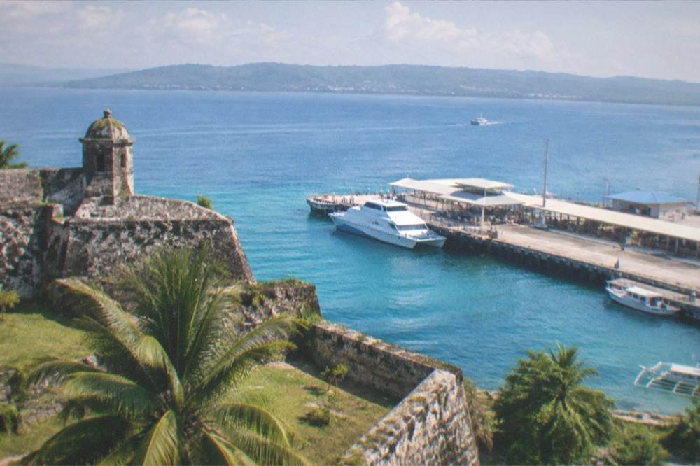 A historic stone fort with thick coral walls overlooking a harbor at morning