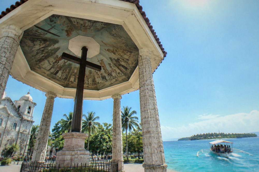 A wooden boat loaded with snorkellers heading toward turquoise water at an island off Cebu