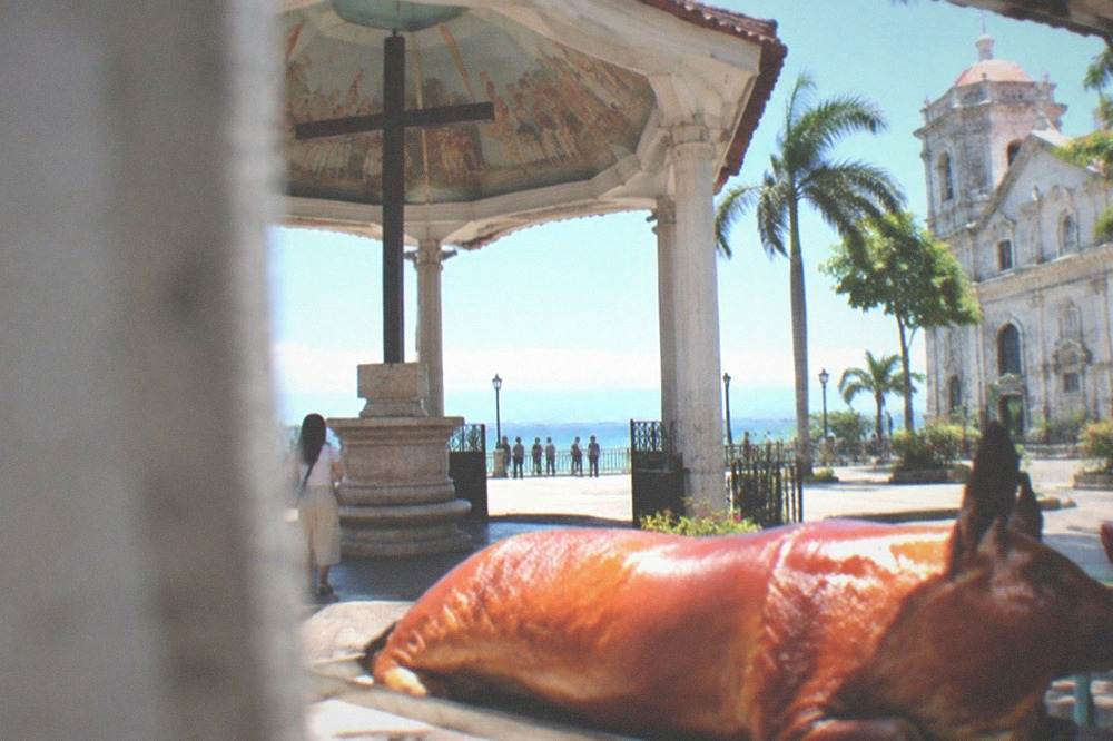 A whole roasted lechon pig with crisp golden skin on a market stall counter in Cebu