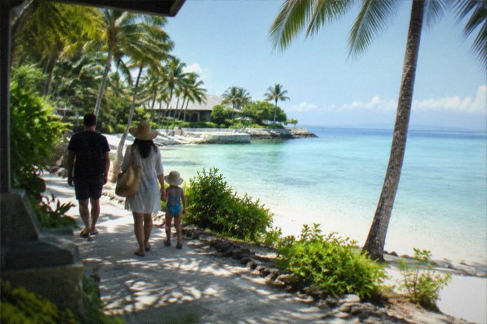 A family walking along a resort beachfront path with calm shallow water on Mactan island