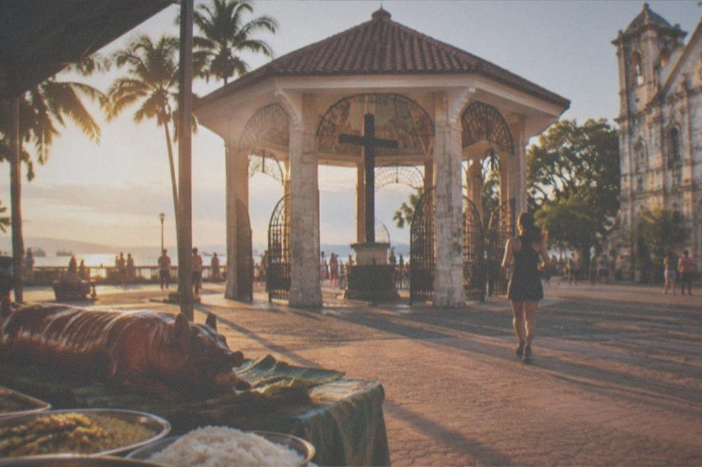 Whole roast pig lechon on a table with rice dishes at an outdoor Philippine market stall
