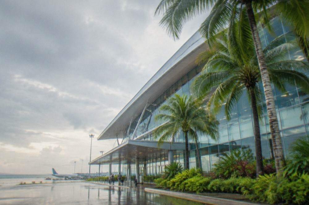 A modern airport terminal glass facade with palm trees in the foreground