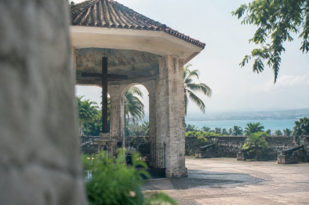 A historic coral-stone fort wall with cannons facing a plaza in a tropical city