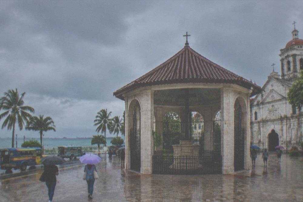 Travelers with umbrellas walking through a wet Cebu street with jeepneys passing