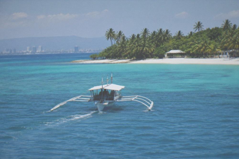An outrigger bangka boat approaching a white sand island beach in the Visayas