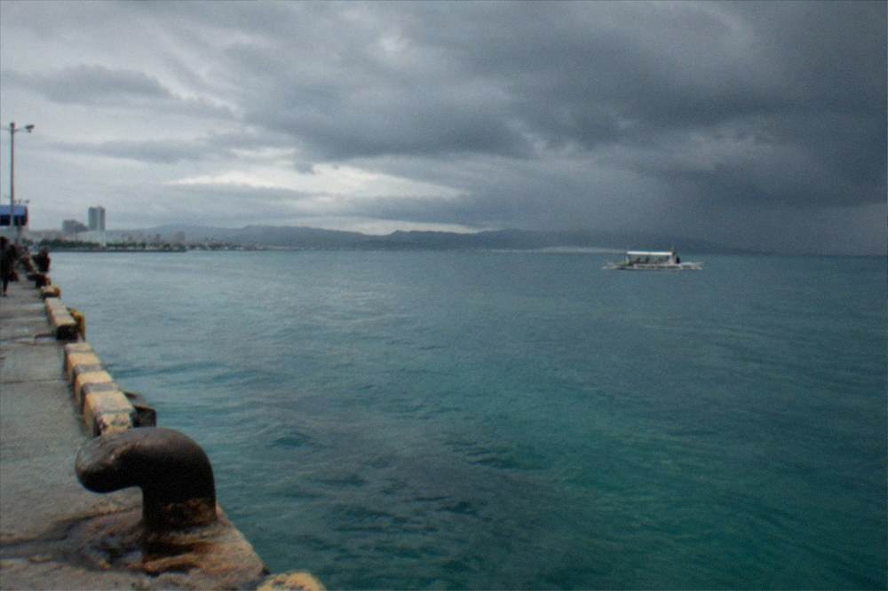 Dark storm clouds gathering over a calm Visayas sea with a small boat in the distance