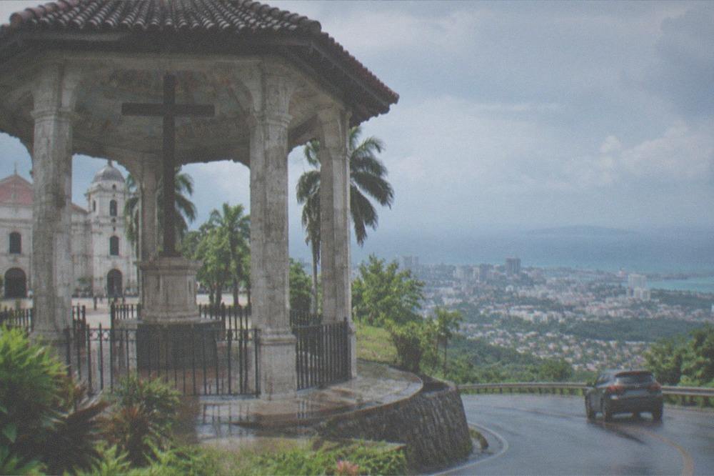 A car winding up a mountain road with a view over Cebu City and the sea