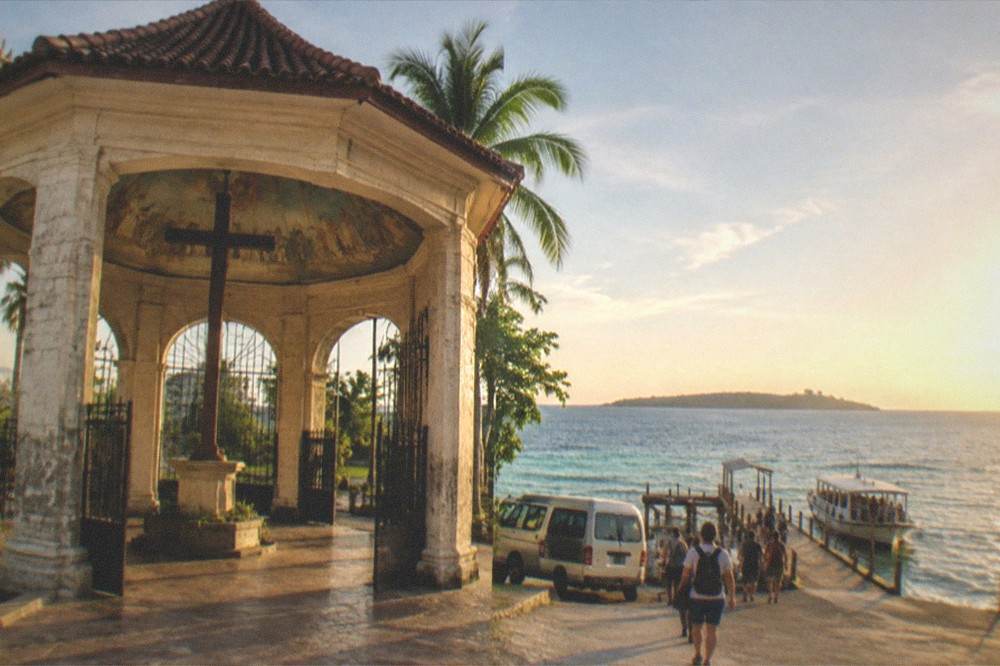 A van of tourists arriving at a wooden pier where a boat waits near an island