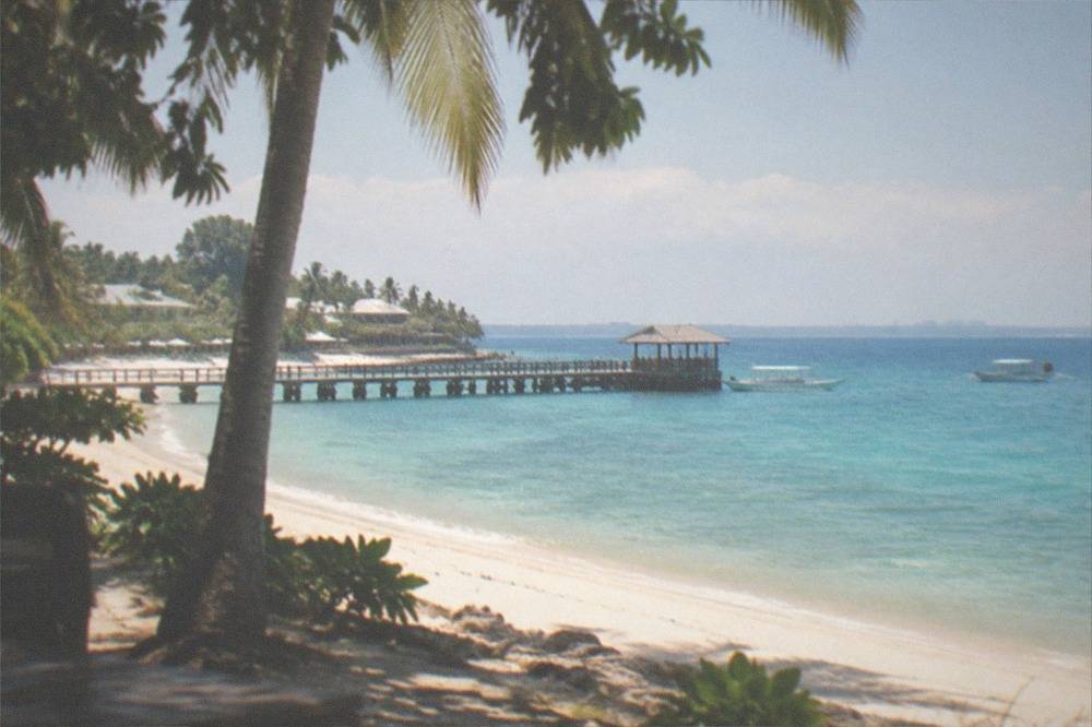 A white sandy beach with a wooden pier and small boats in clear water on Mactan