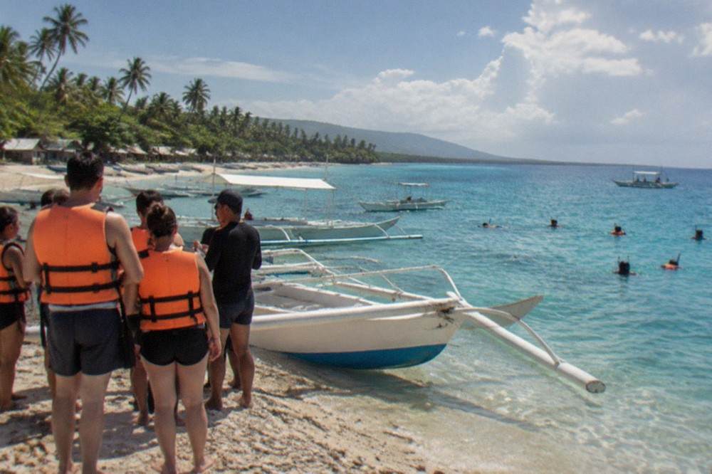 Tourists in life jackets listening to a briefing beside outrigger boats on the beach at Tan-awan, Oslob