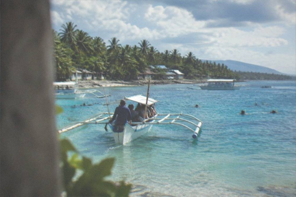 An outrigger boat returning to shore in the morning light at Tan-awan, Oslob