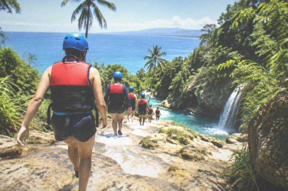 Canyoneers in helmets and life vests descending a canyon stream toward Kawasan Falls