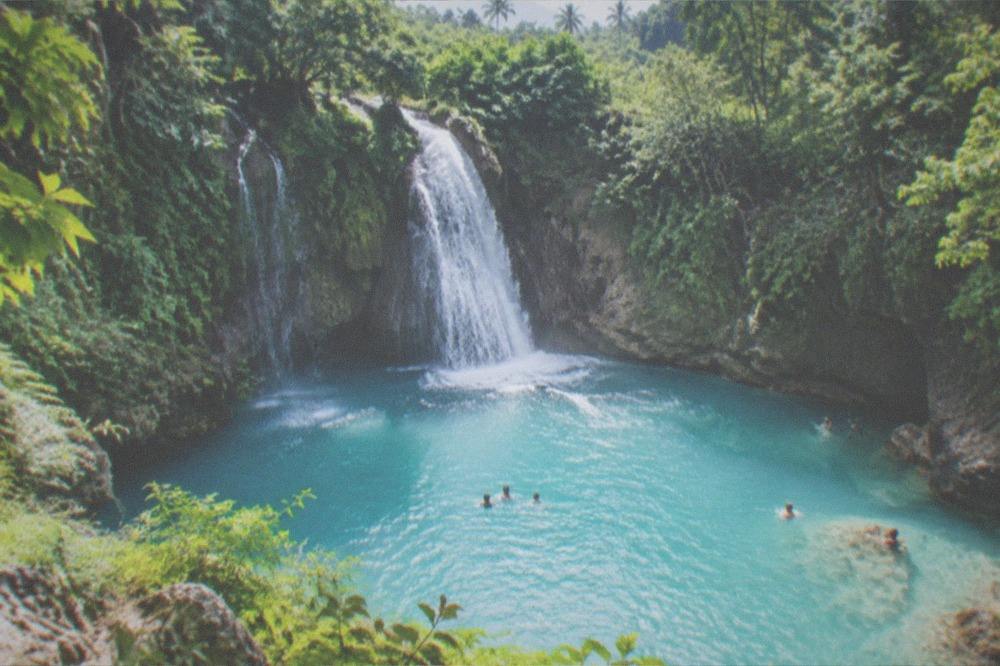 A waterfall dropping into a turquoise pool surrounded by jungle at Kawasan Falls, Cebu
