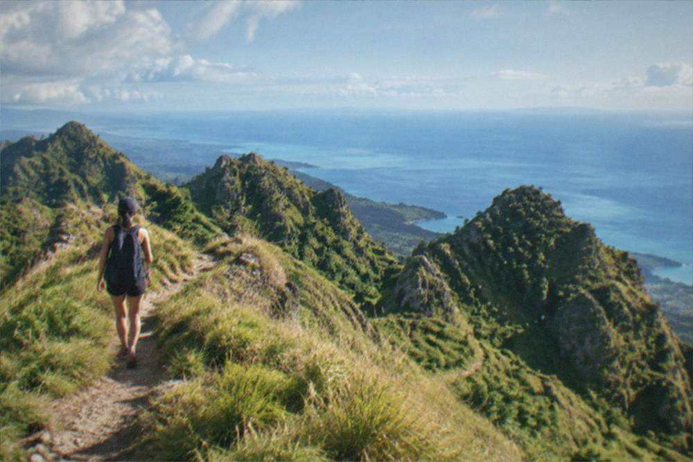 A hiker on a grassy ridge trail above the coastline at Osmeña Peak, Cebu