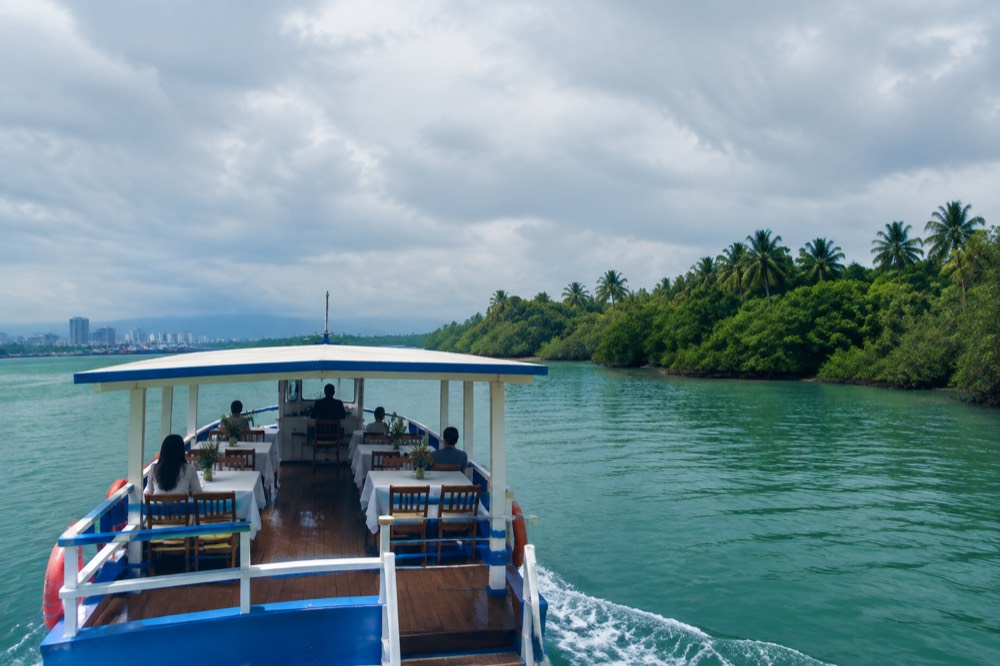 A small boat cruising on a green jungle river with lunch tables set on deck