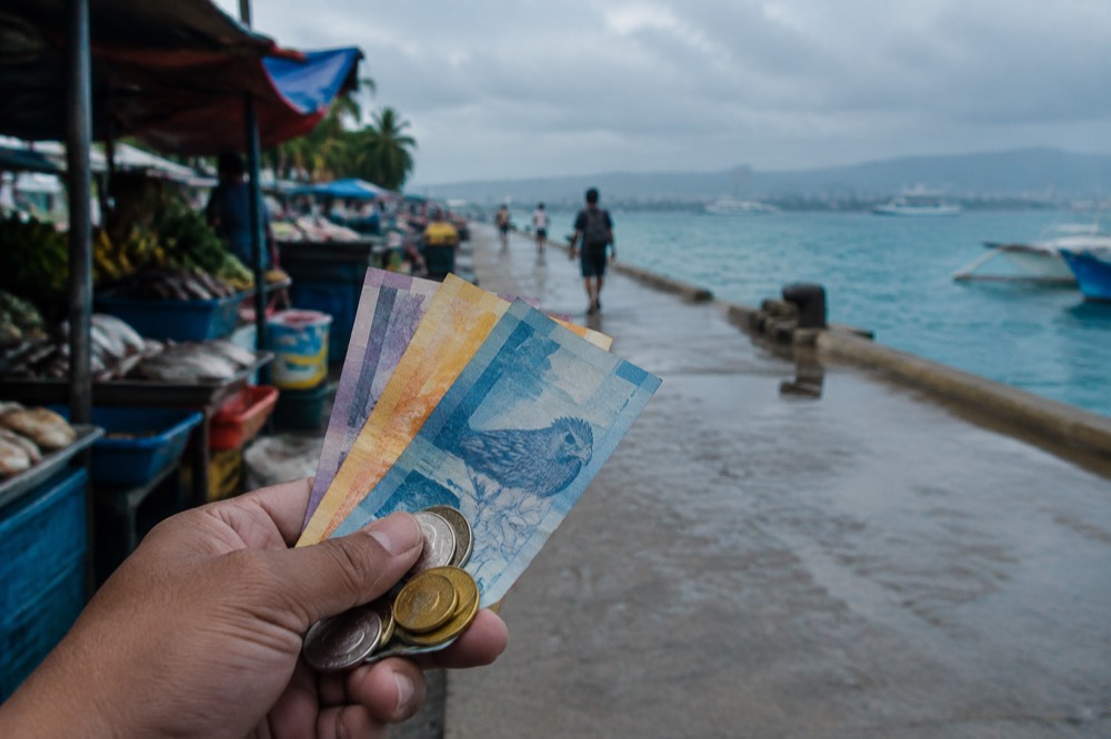 Fresh Philippine peso banknotes and small coins held in a hand at a market stall