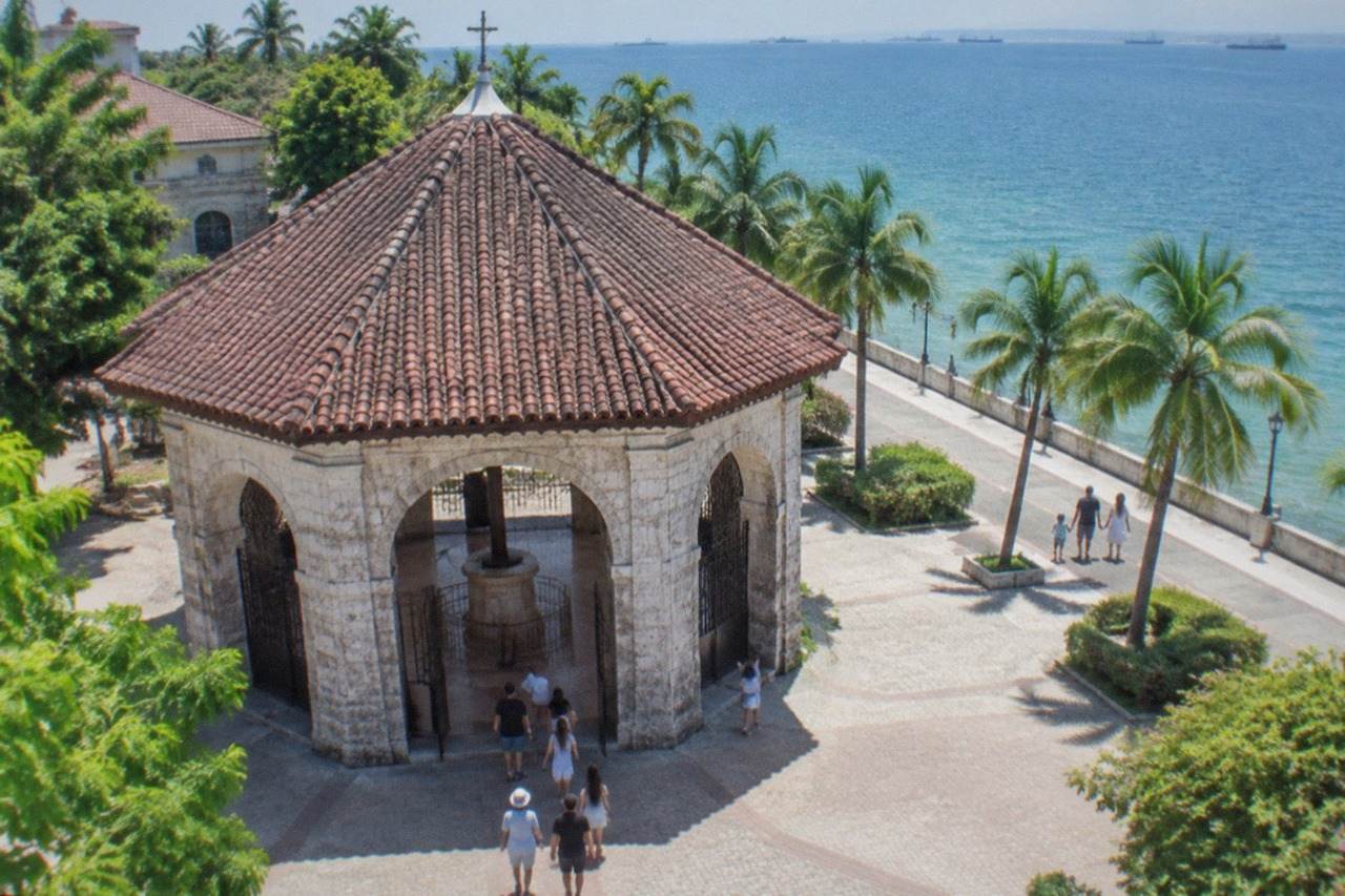 A family walking along a seaside promenade in Cebu with palm trees and calm water
