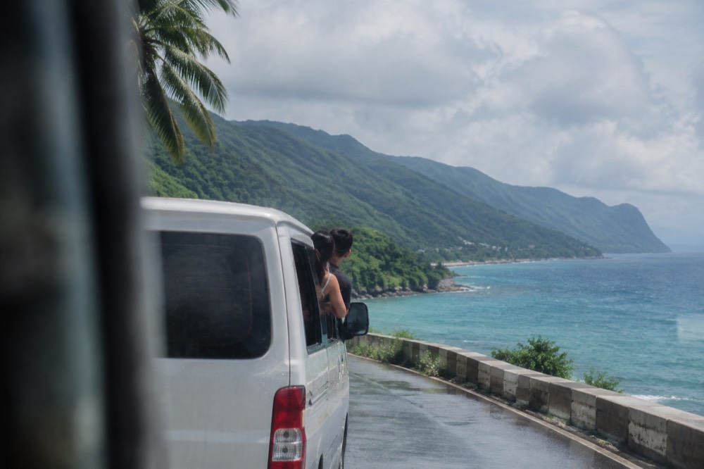 A couple riding a private van along a coastal road with green mountains in Cebu