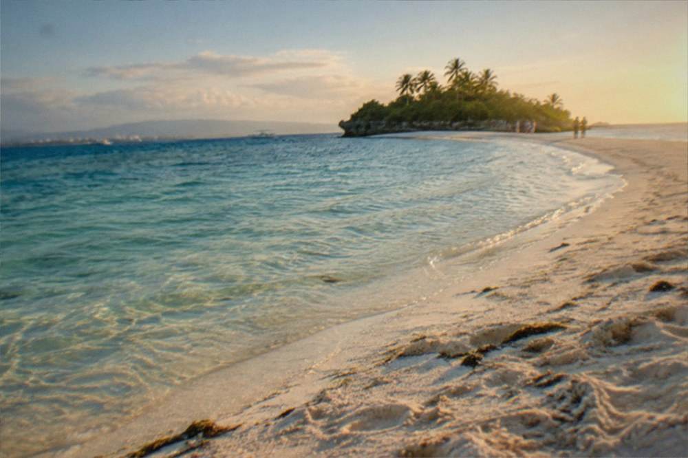 A white sandbar curving into clear shallow water with a small island behind it